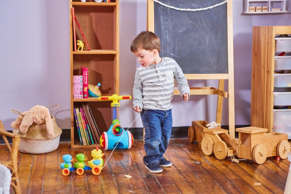Child playing with toys in a room with wooden floor and bookshelf.