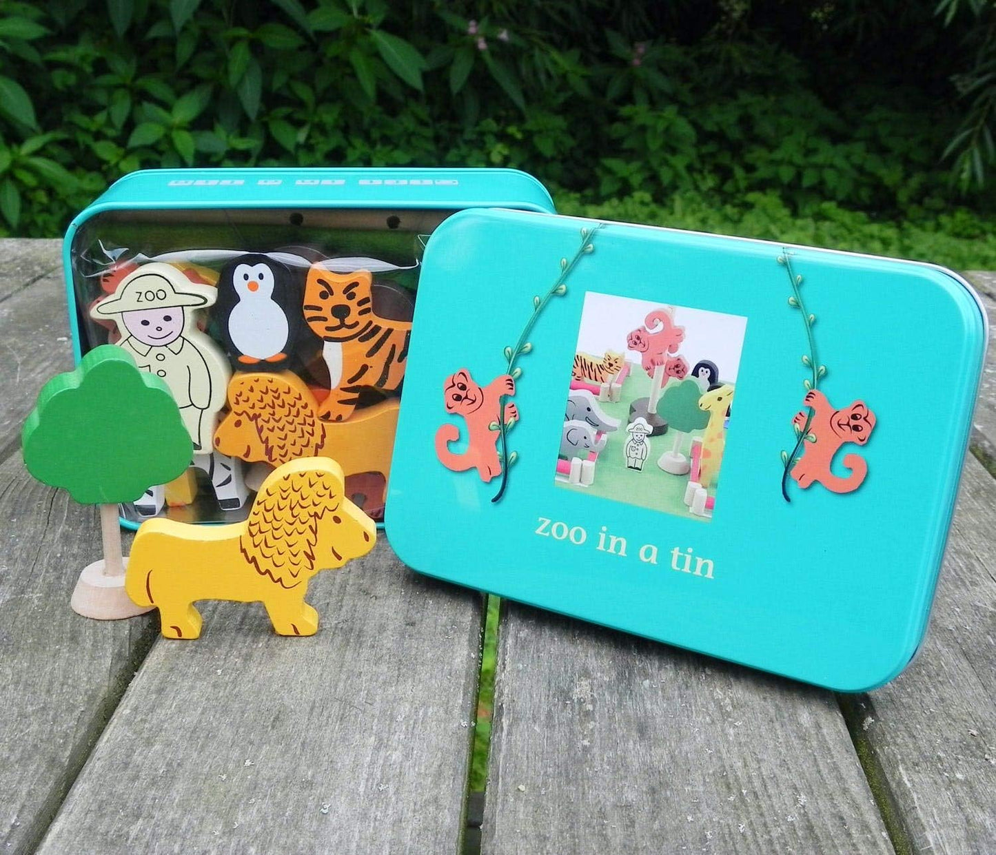 Teal toy box labeled 'zoo in a tin' with wooden animal figures on a wooden surface.