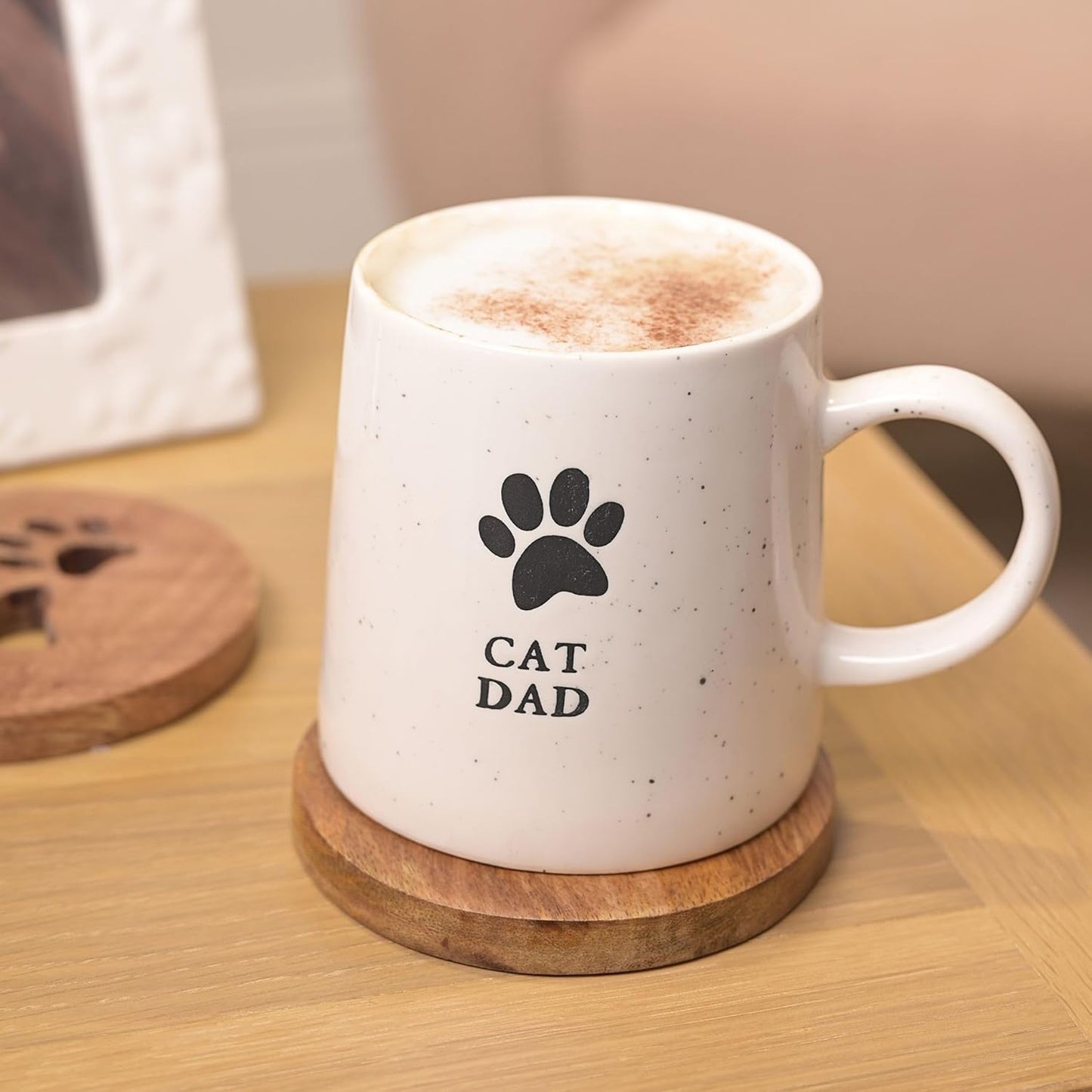 White mug with 'Cat Dad' and paw print design on a wooden coaster.