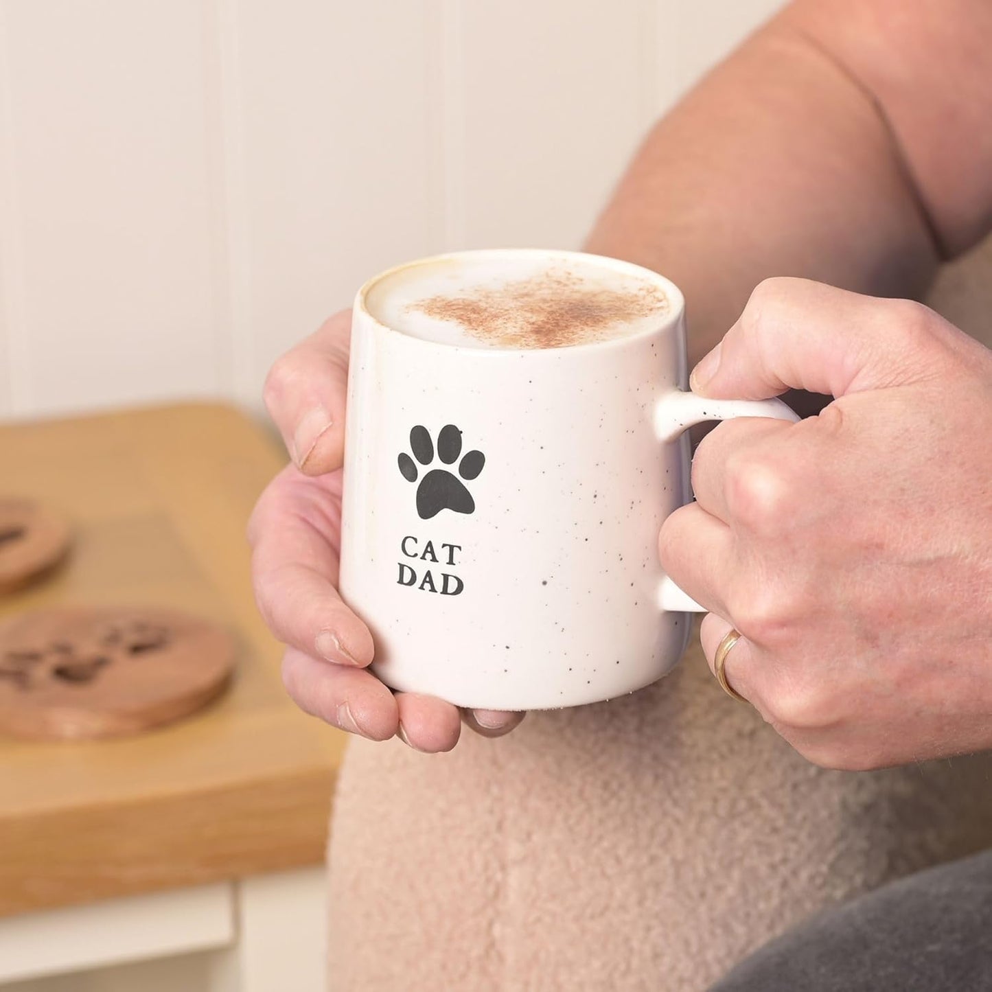 Person holding a mug with 'Cat Dad' text and paw print design, with a blurred background.