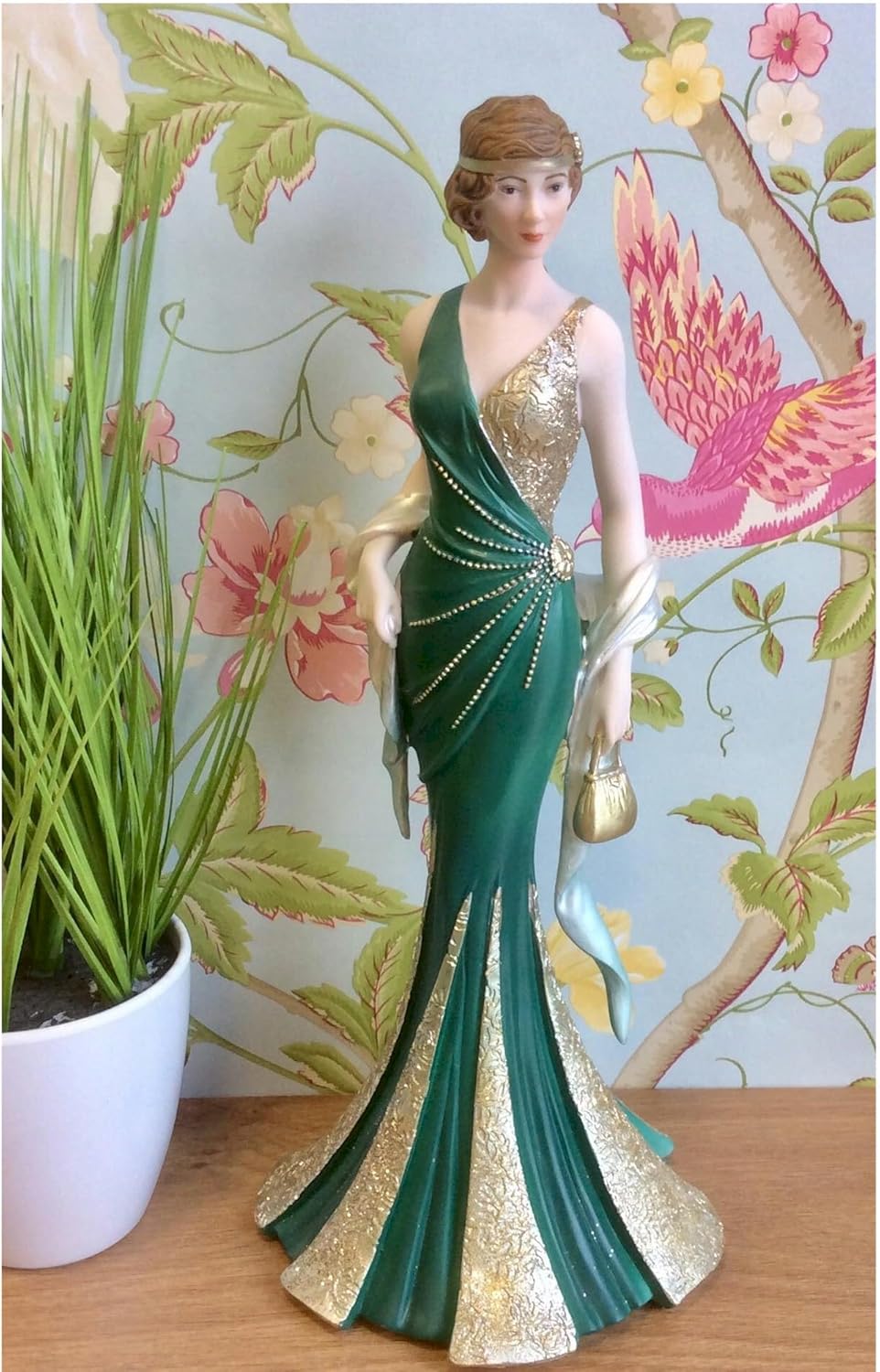 Decorative figurine of a woman in a green and gold dress against a floral background