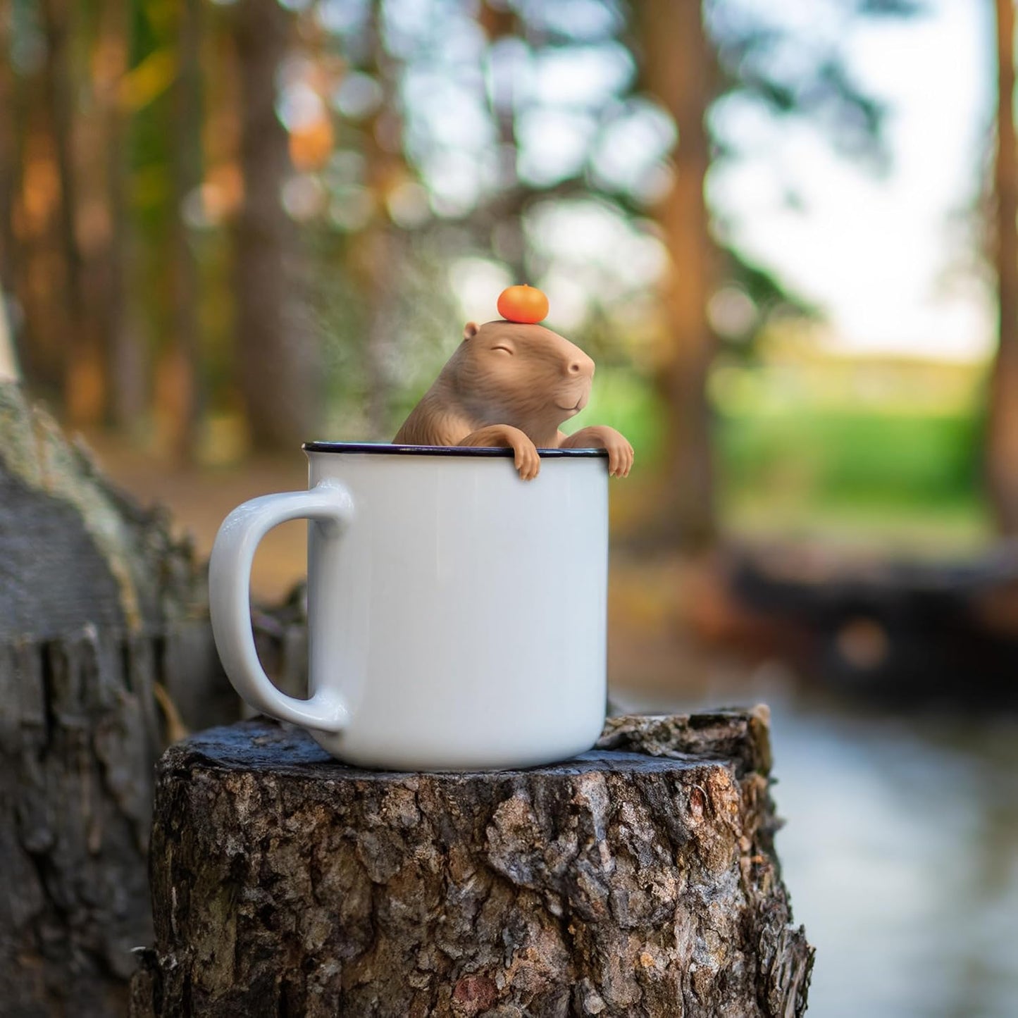 Small figurine of a capybara on top of a white mug with a blurred natural background