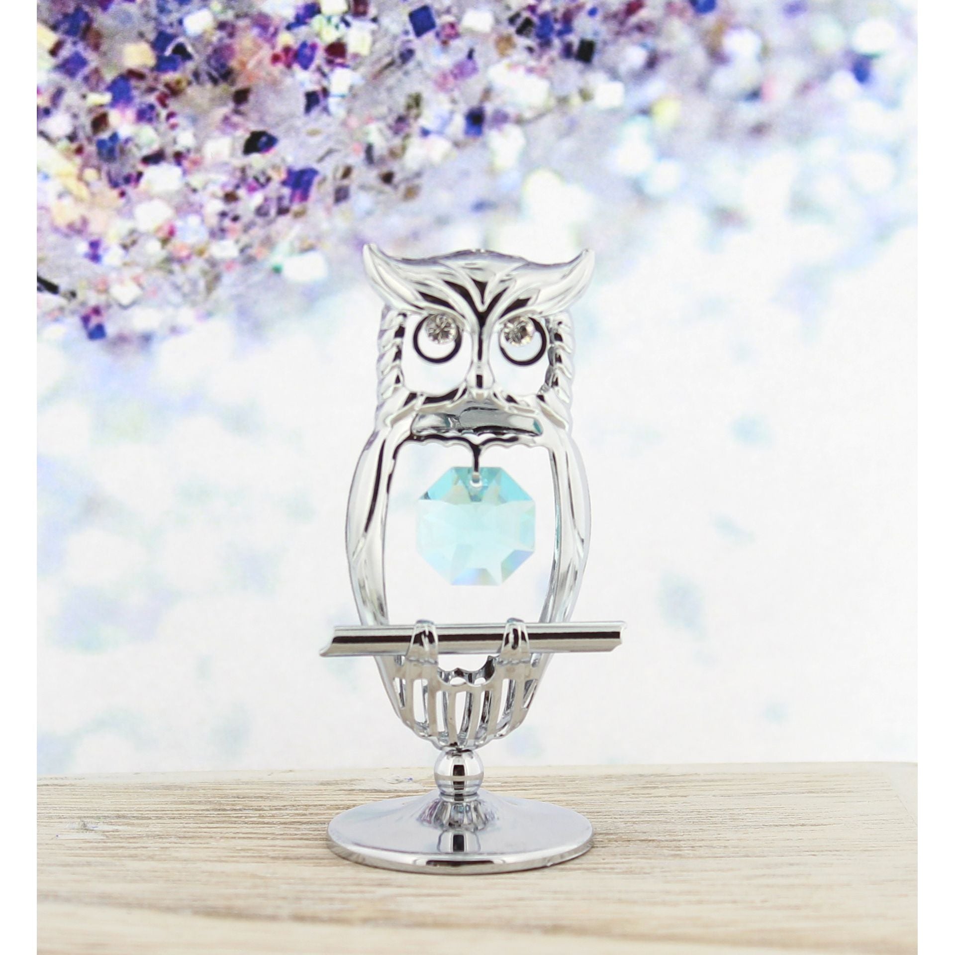 A silver chrome plated owl ornament with a blue aqua marine crystal embellishment in its nest.