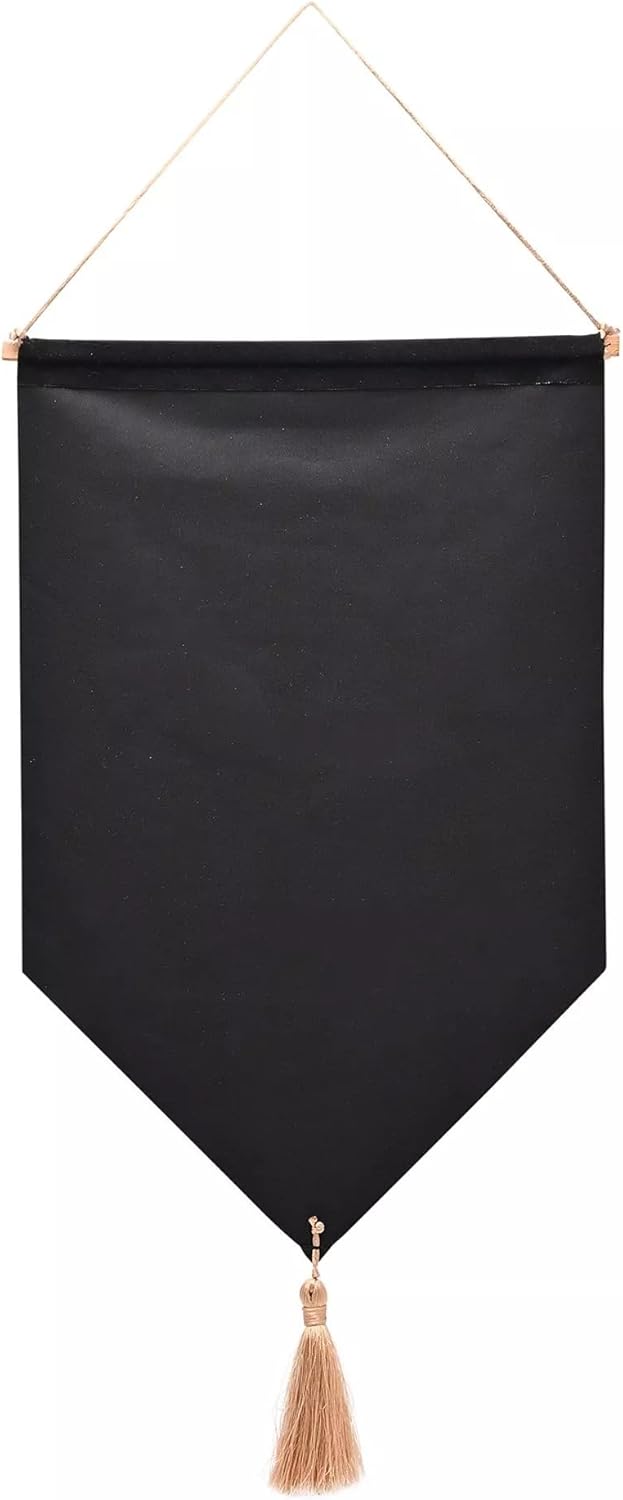 A black fabric wall hanging banner with a pointed bottom and a beige tassel, suspended by a thin beige cord with gold-toned metal rings, shown against a plain white background.