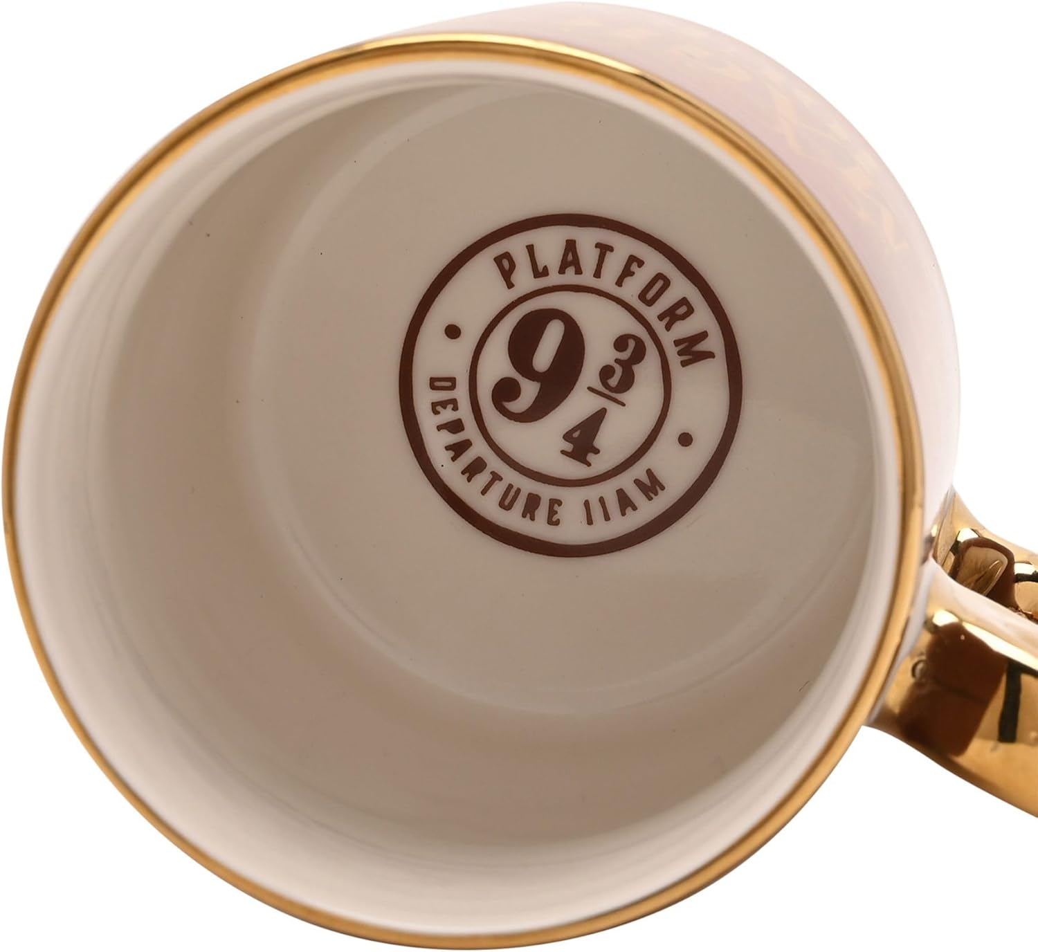Close-up of the inside of a ceramic mug showing a printed circular stamp that reads 'PLATFORM 9 3/4 DEPARTURE ILIA' in dark brown on a warm off-white background, with a gold rim and gold handle visible.