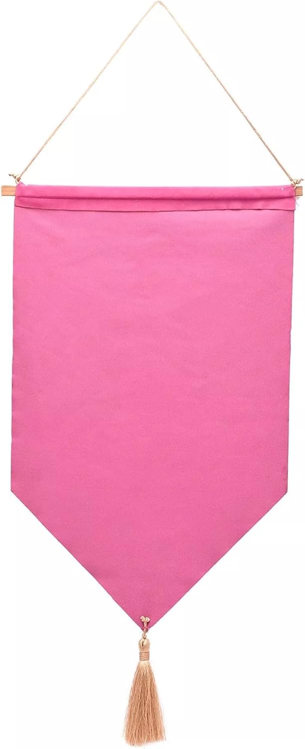A bright pink fabric wall hanging banner with a pointed bottom and a beige tassel, suspended by a thin cord against a white background.
