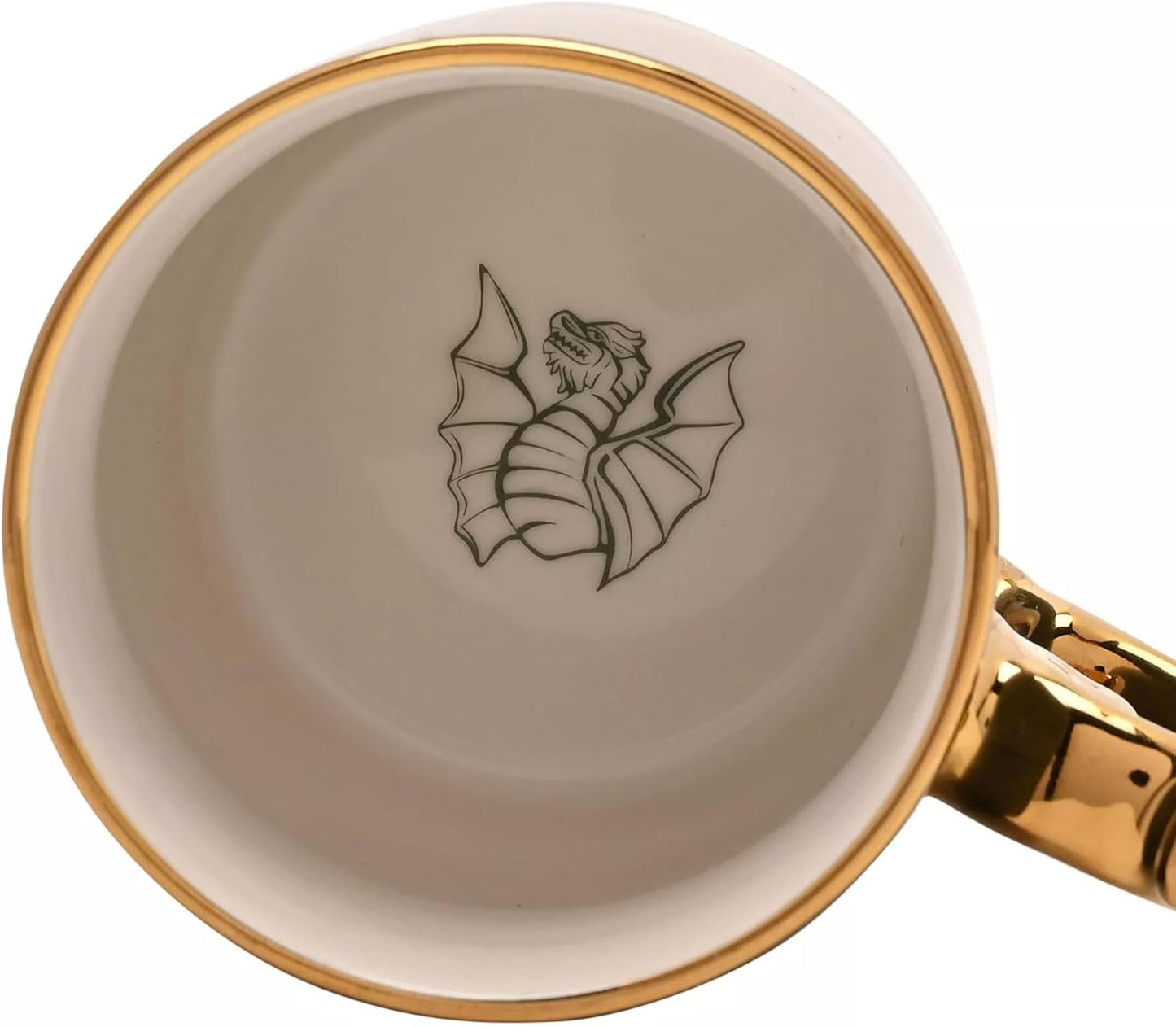 Close-up of the inside of a white ceramic mug with a shiny gold rim, a gold handle, and a black line-art illustration of a dragon on the bottom.