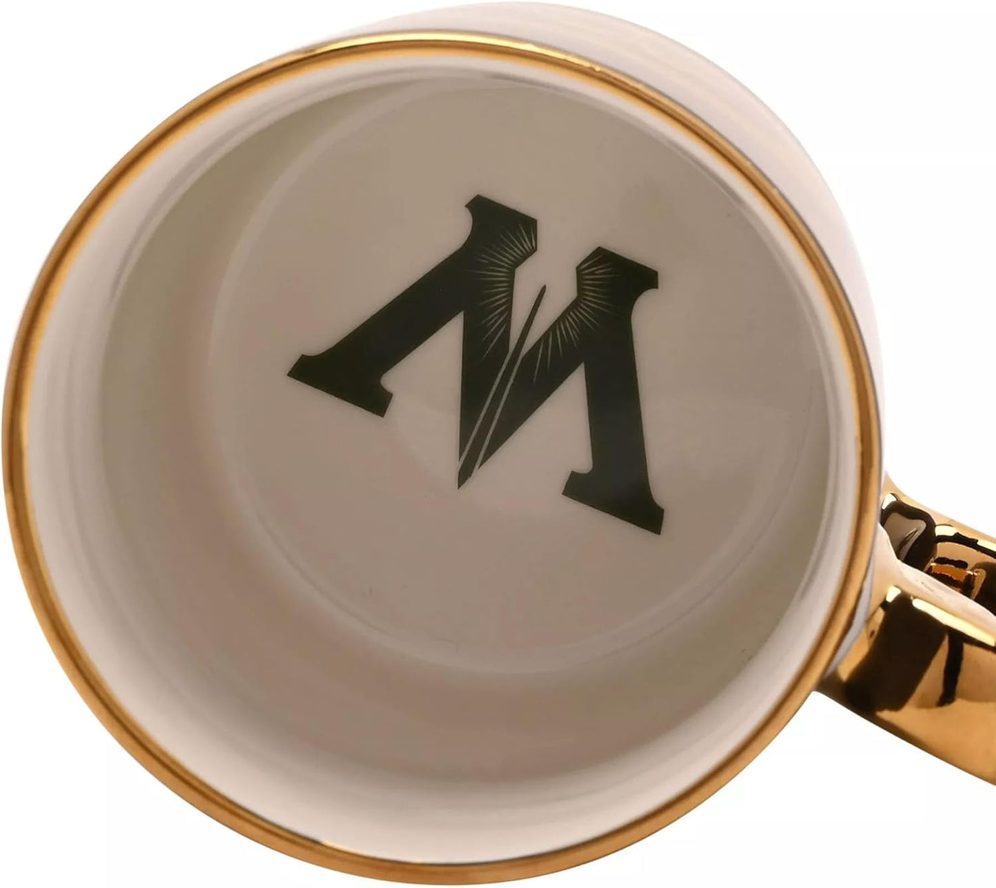 Close-up of a ceramic mug showing the inside of the cup with a gold rim, a black monogram letter 'M' printed in the center, and part of a shiny gold handle visible on the right.