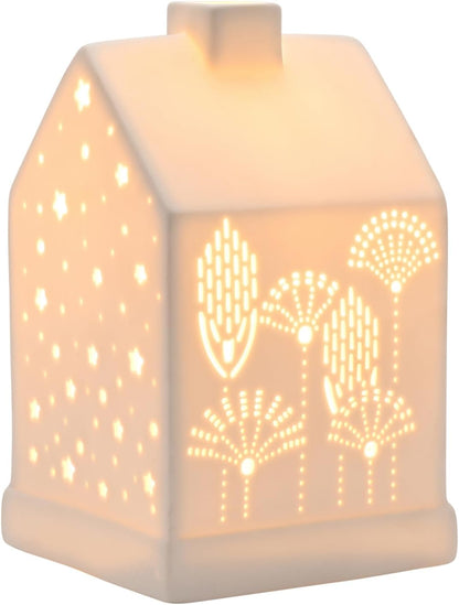 A small house-shaped ceramic night light glowing with warm light, featuring laser-cut star and leaf patterns on the front and side.