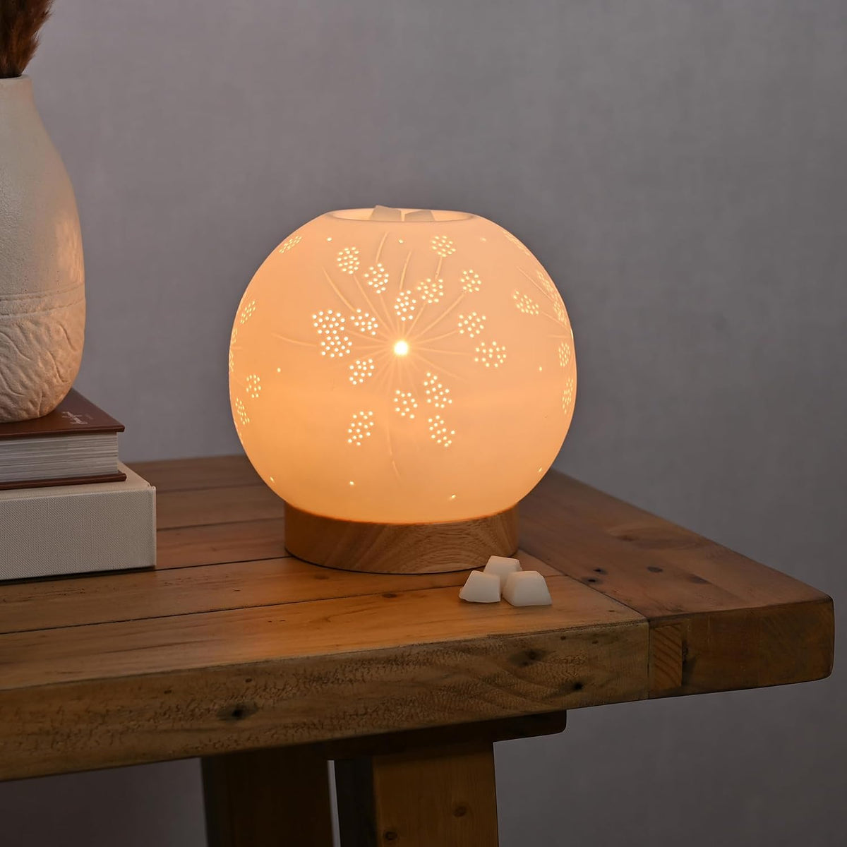 Decorative lamp on a wooden table with a soft glow and wax melts infront