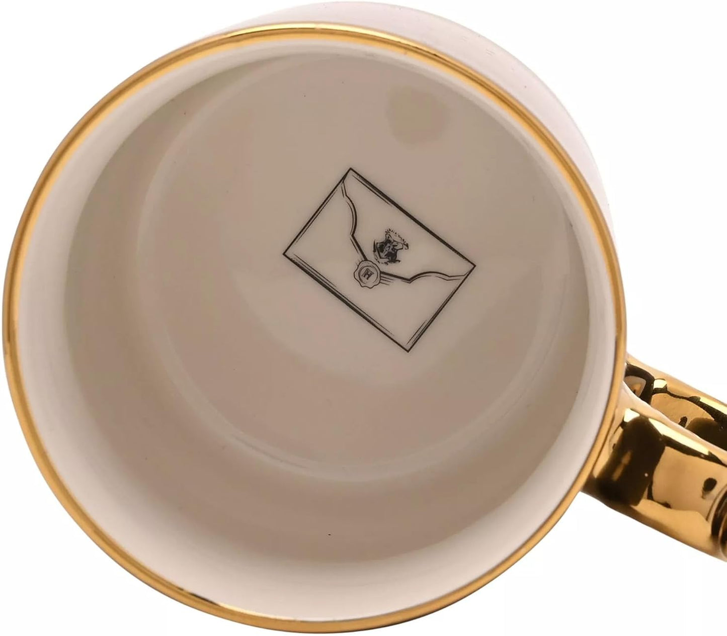 Close-up of the inside of a white ceramic mug with a gold rim and a gold handle, featuring a black printed envelope logo on the bottom.
