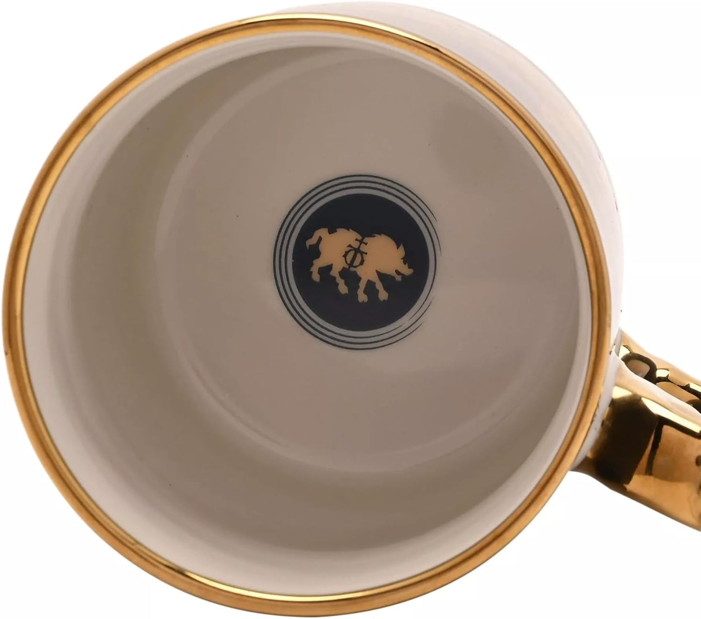 Close-up of the inside of a ceramic mug showing a cream-colored interior, a gold rim, a gold handle, and a central dark blue circular logo with a gold boar silhouette.