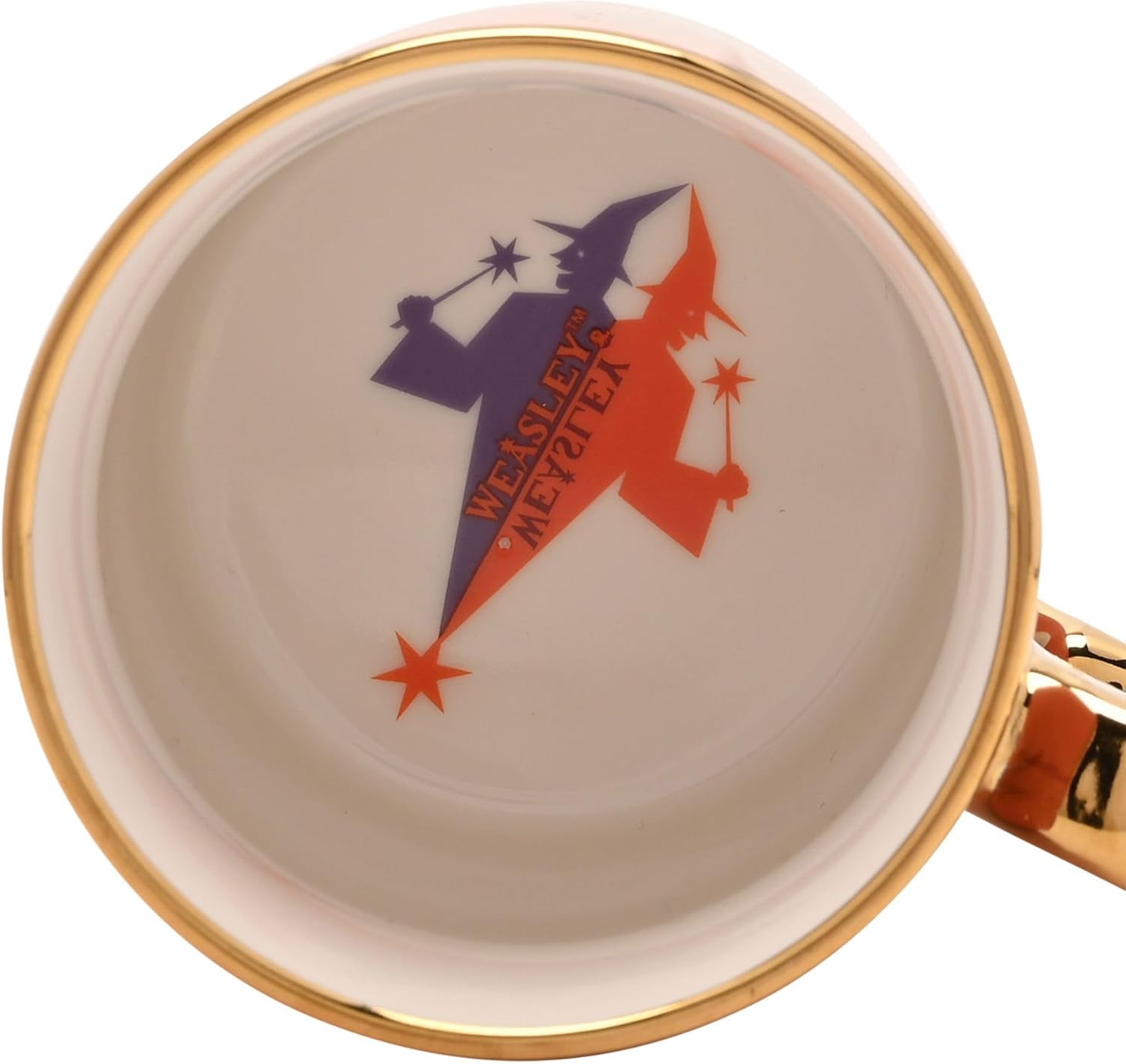 Close-up of a white ceramic mug interior with a gold rim, featuring a retro-style graphic of two witches in purple and orange with the text 'WEALSLEY'