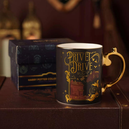 A dark navy blue Harry Potter collectible mug with gold foil detailing reading 'Privet Drive No 4' and a gold handle, shown next to its branded box on a brown leather surface.