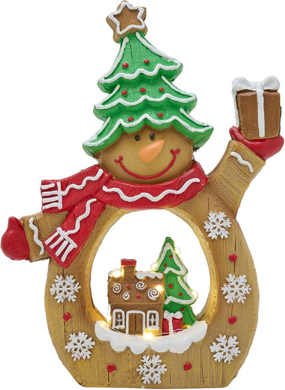 A festive snowman gingerbread decoration with a green Christmas tree hat, red and white striped scarf, and a warm wooden body featuring a glowing holiday village scene inside.