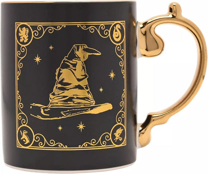 A black ceramic mug with a metallic gold handle and a gold printed design featuring a pointed hat, stars, and ornate borders, shown on a white background.