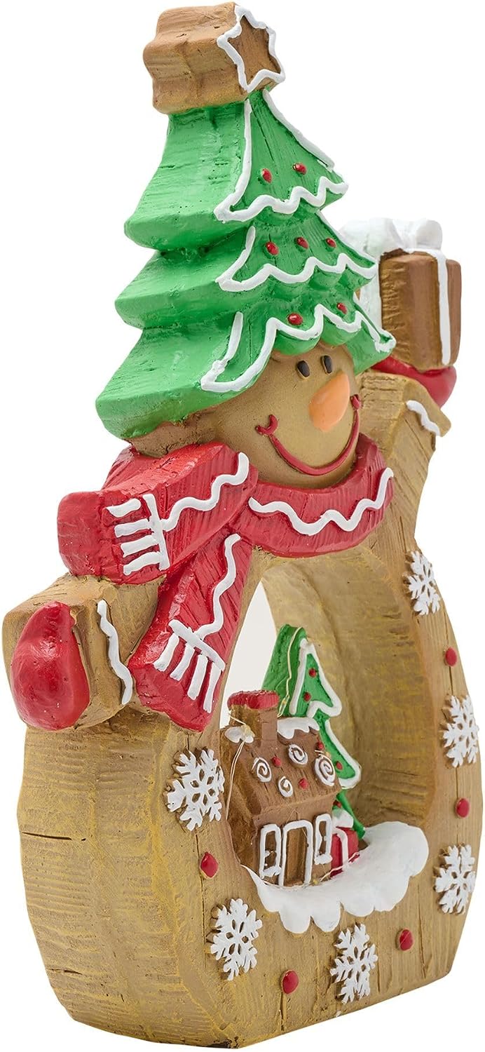 A decorative gingerbread-themed snowman ornament holding a green Christmas tree and a gift box, with a red scarf and white snowflake details on a plain white background.
