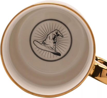 Top-down view of a ceramic mug showing a cream-colored interior with a black illustration of a wizard hat inside a circular frame, accented by a gold rim and a gold handle.