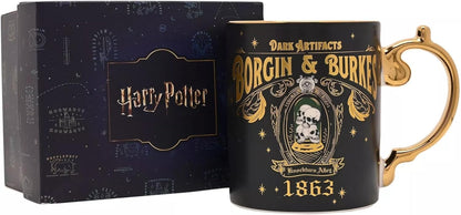 A Harry Potter Dark Artifacts Borgin & Burken ceramic mug with a gold handle, shown next to its dark blue presentation box featuring the Harry Potter logo.