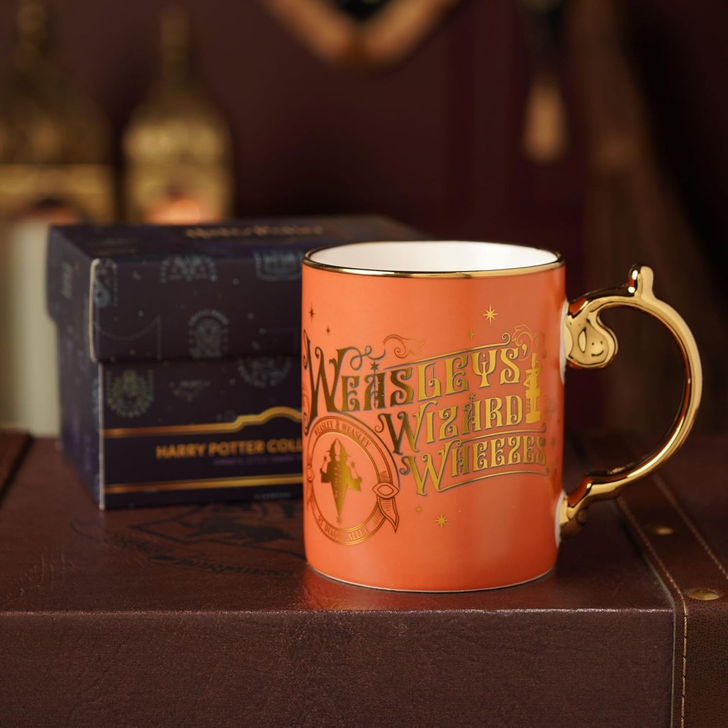 Orange mug with gold text 'Weasley's Wizard Wheezes' on a wooden surface with a box in the background.