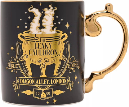 A black ceramic mug with a metallic gold handle and gold printed design featuring 'The Leaky Cauldron' from Harry Potter, including a cauldron, dragon, house number 15, and the text 'Diagon Alley, London'.