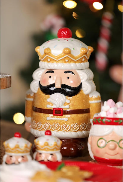 A ceramic Christmas nutcracker figurine with a gold and white outfit, black mustache, and red crown accent, shown in a festive holiday setting with blurred lights and other holiday decorations.