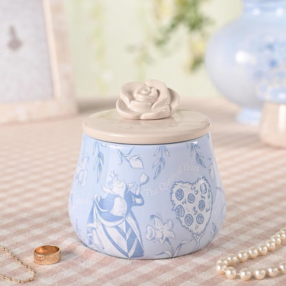 Decorative jar with a rose-shaped lid on a textured surface with jewelry.