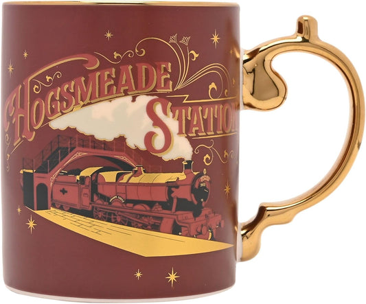 A ceramic mug featuring a Hogsmeade Station theme from Harry Potter, with a dark red body, gold handle and trim, and an illustration of a train and station architecture.