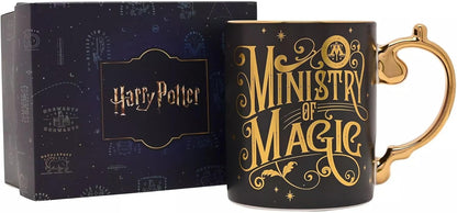 A black ceramic Harry Potter 'Ministry of Magic' mug with gold lettering and a gold handle, shown next to its dark blue branded gift box.