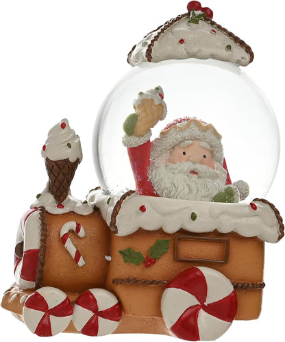 A festive gingerbread-themed snow globe figurine featuring Santa Claus inside a clear glass dome, with a train design decorated like a gingerbread house, candy canes, peppermint wheels, and ice cream cones on a white background.