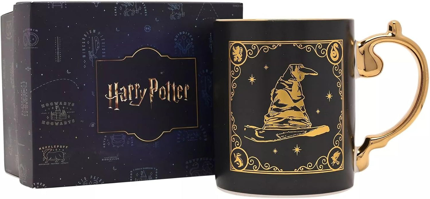 A black ceramic Harry Potter mug with a gold printed illustration of a wizard hat on a broomstick, shown next to its dark blue branded gift box.