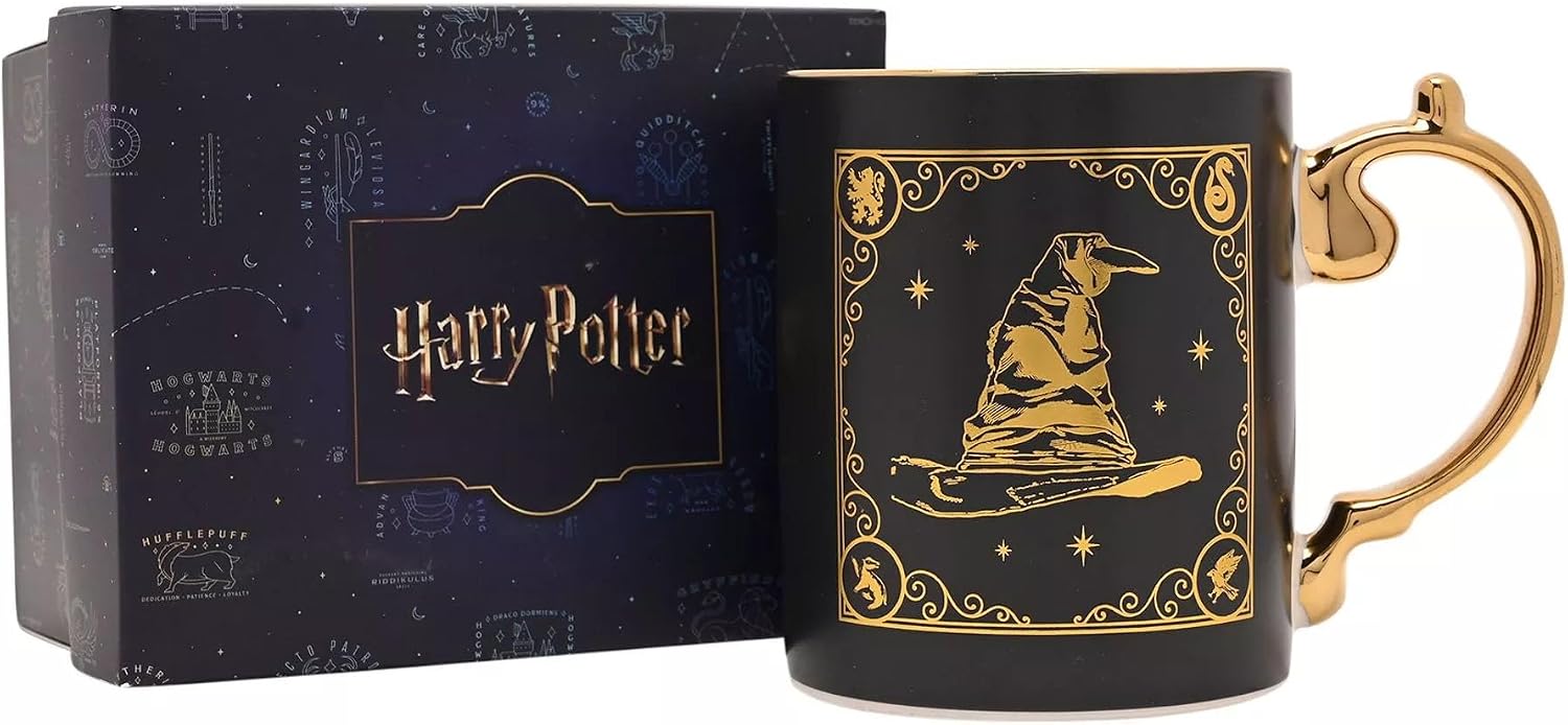 A black ceramic Harry Potter mug with a gold printed illustration of a wizard hat on a broomstick, shown next to its dark blue branded gift box.