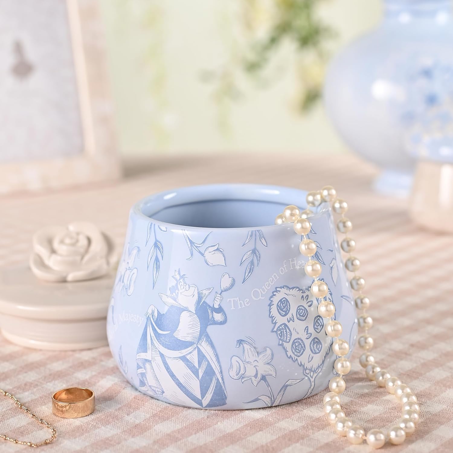 Blue ceramic pot with white floral design on a textured surface with a pearl necklace.
