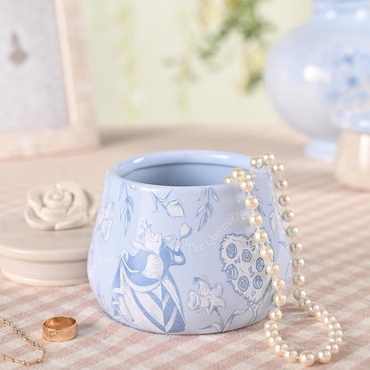 Blue ceramic pot with white floral design on a textured surface with a pearl necklace.
