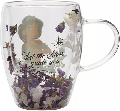 A clear glass mug featuring a printed illustration of Jasmine from Aladdin, the phrase 'Let the Stars guide you' in black script, and dried purple and white flowers embedded inside the glass.