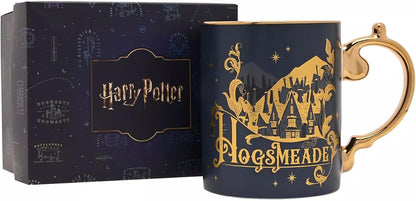 A dark navy blue Harry Potter Hogsmeade ceramic mug with gold detailing and a gold handle, shown next to its branded dark blue gift box.