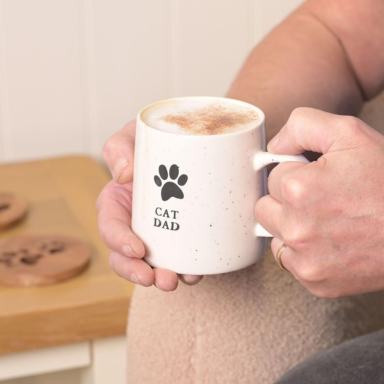 Person holding a mug with 'Cat Dad' text and paw print design, with a blurred background.