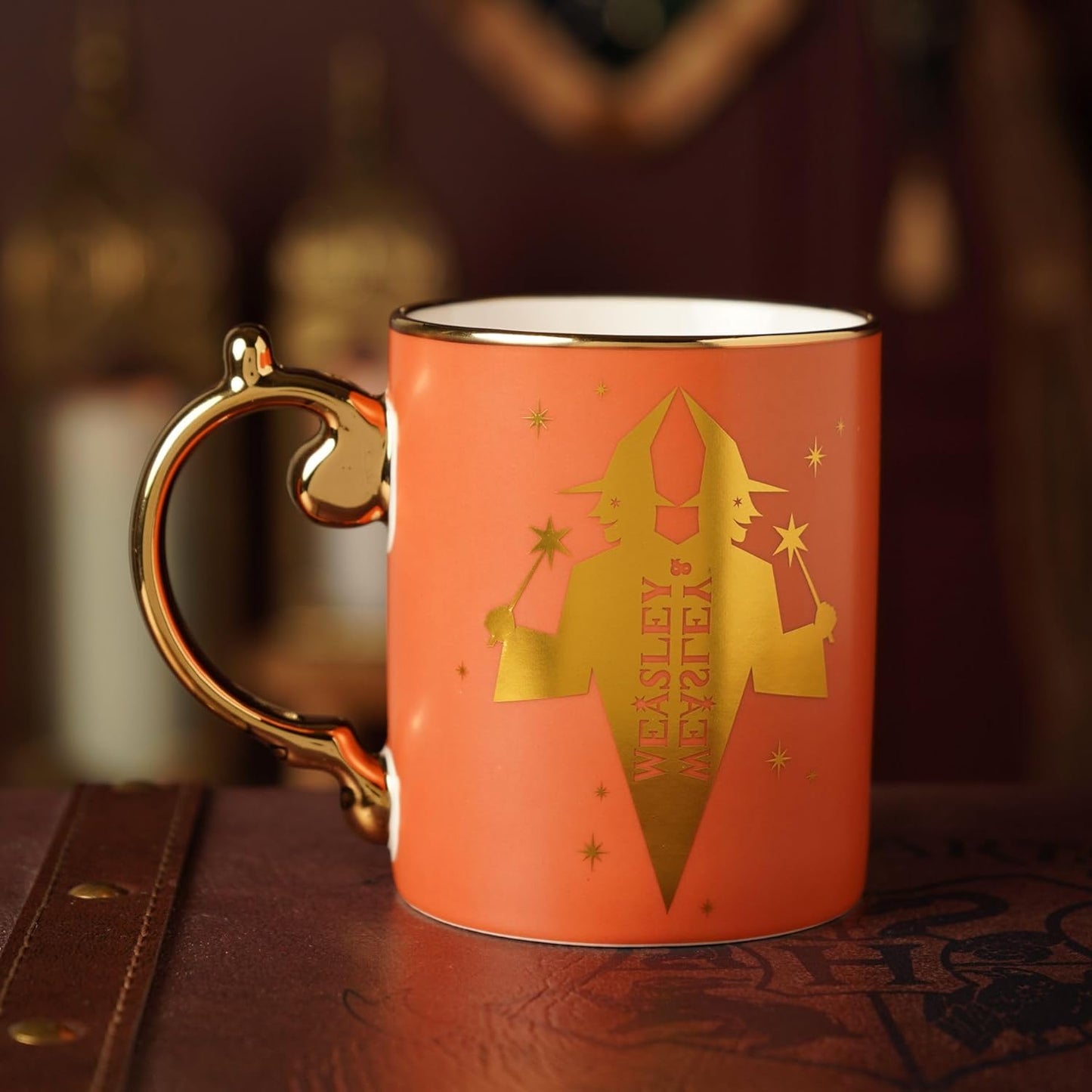 Orange mug with gold handle and 'Weasley Wizard Wheezes' logo on a dark surface