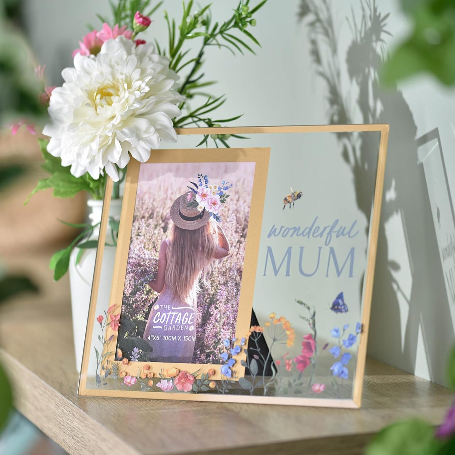 Decorative photo frame with floral design on a shelf with flowers in the background