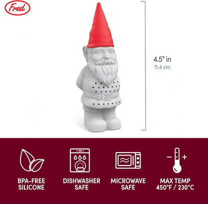 Tea infuser shaped like a gnome in a glass of tea on a wooden table with plants in the background.