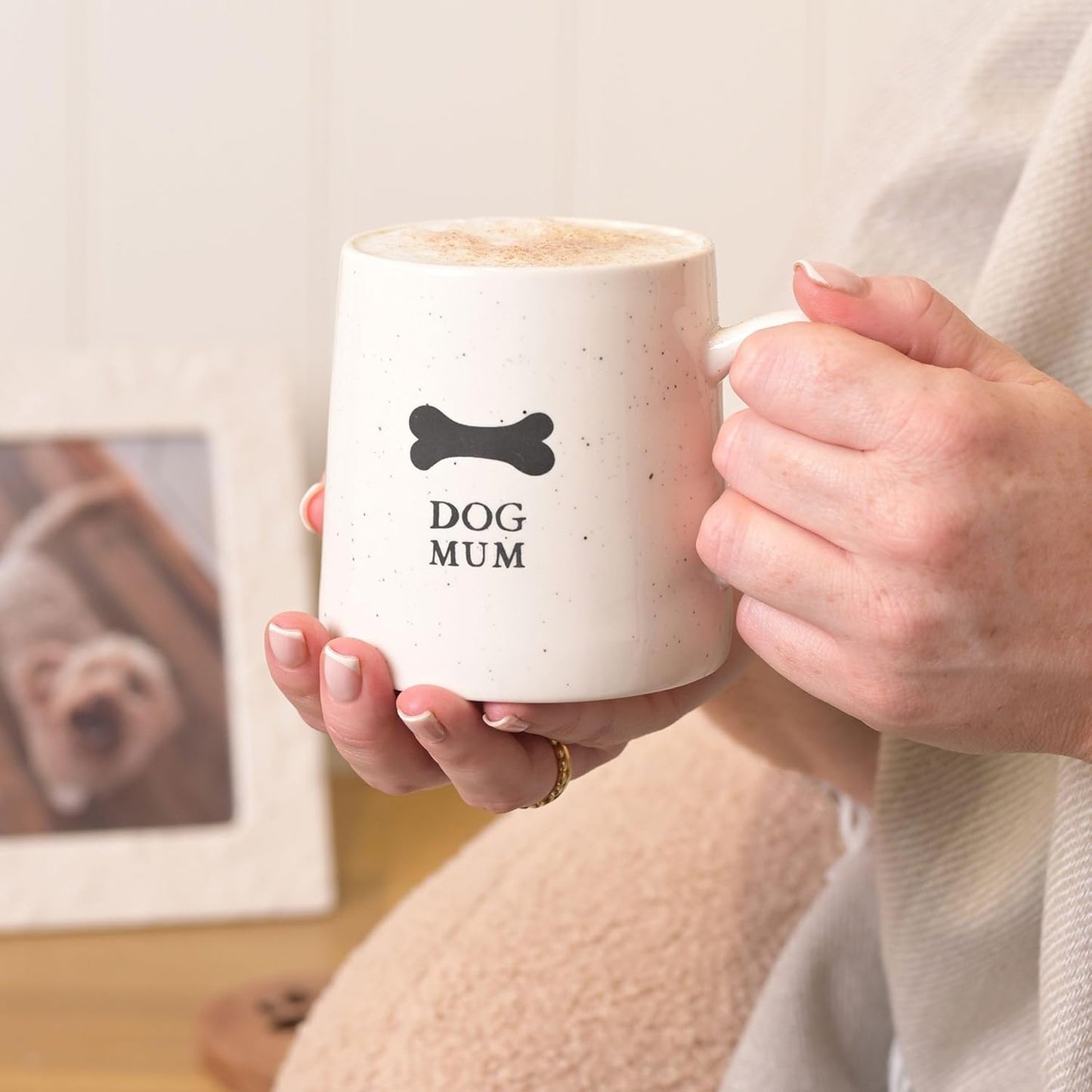 Person holding a mug with 'DOG MUM' text and a bone symbol, sitting on a couch.