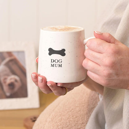 Person holding a mug with 'DOG MUM' text and a bone symbol, sitting on a couch.