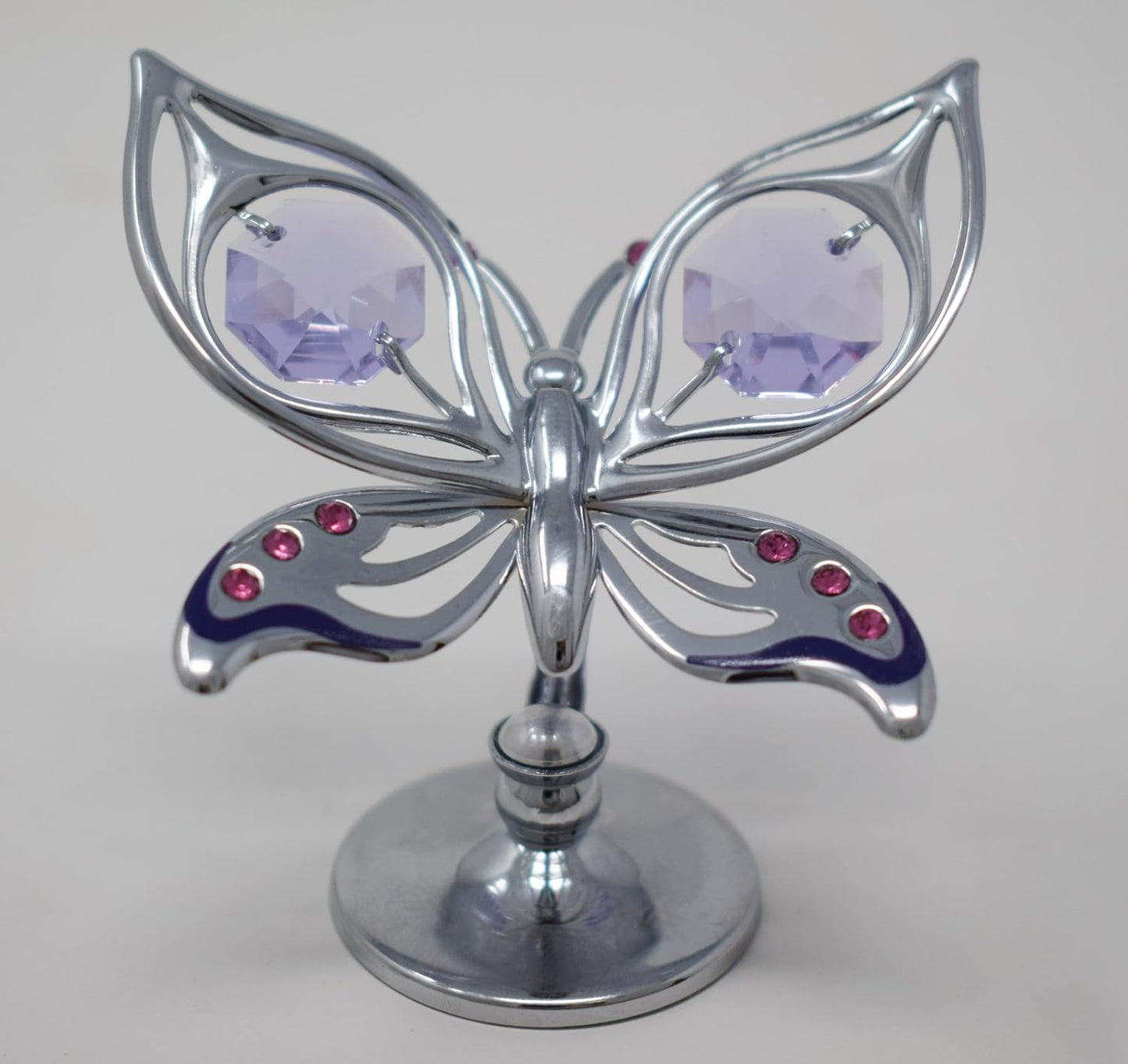 Metallic butterfly ornament with purple and red gemstones on a white background