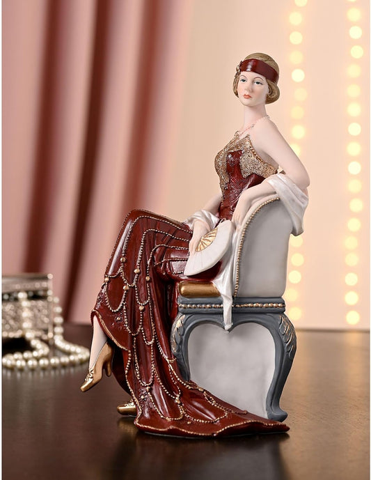 Decorative figurine of a woman in an elegant chair with a draped fabric, against a warm-toned curtain background.