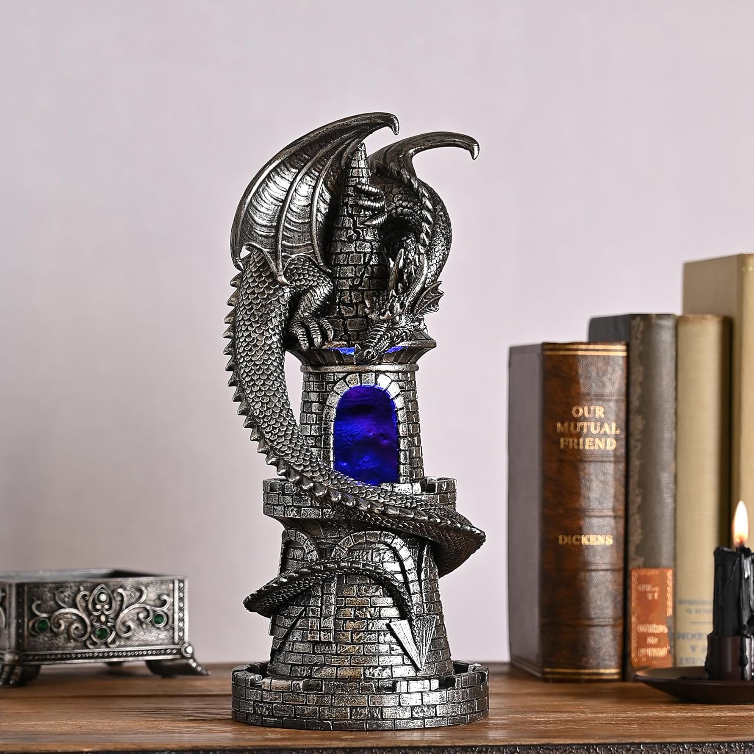 Decorative dragon sculpture with a blue light on a wooden surface with books in the background.