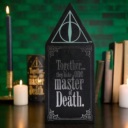 Black tombstone-shaped object with text and symbol, surrounded by candles and books on a green background