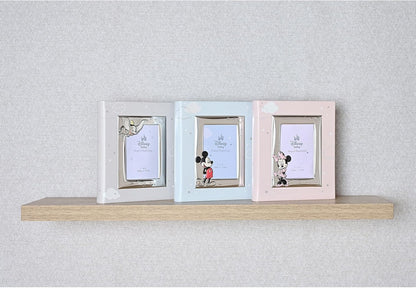 Three pastel-colored picture frames on a wooden shelf against a light gray wall.