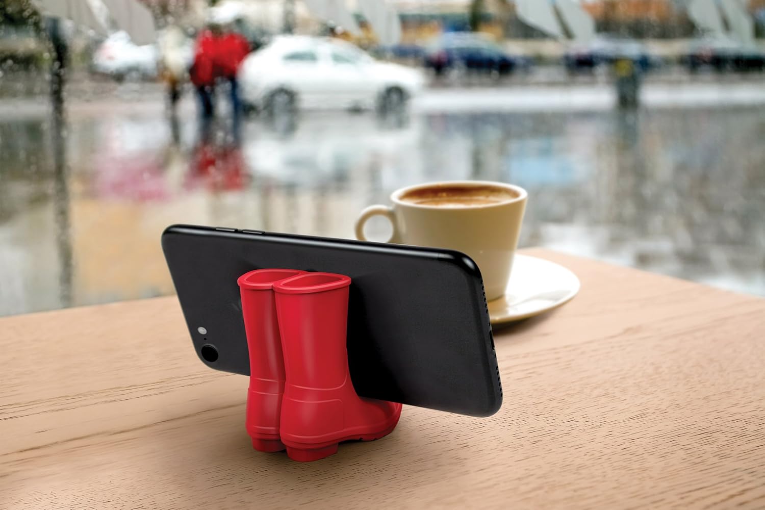 Red phone holder on a table with a smartphone and a cup of coffee in the rain.