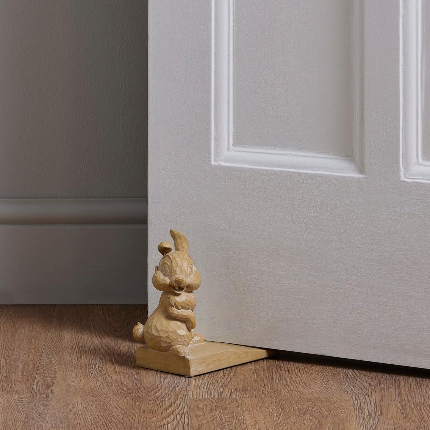 Wooden door stopper shaped like a rabbit on a wooden floor next to a white door.