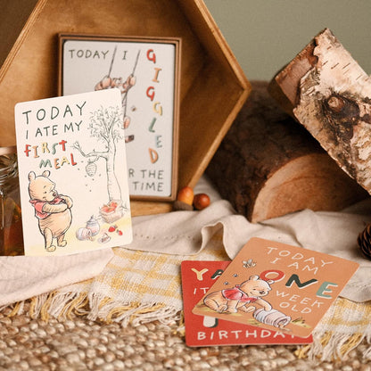 Winnie the Pooh milestone cards on a table with some logs and blankets